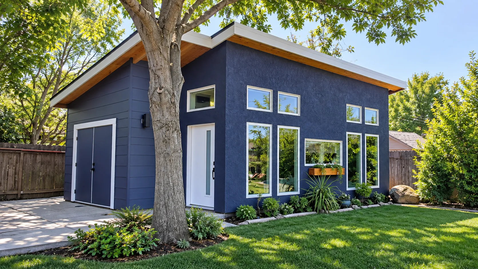 Completed Land Park modern ADU exterior with navy stucco and siding, white trim, and large windows, shaded by a mature tree